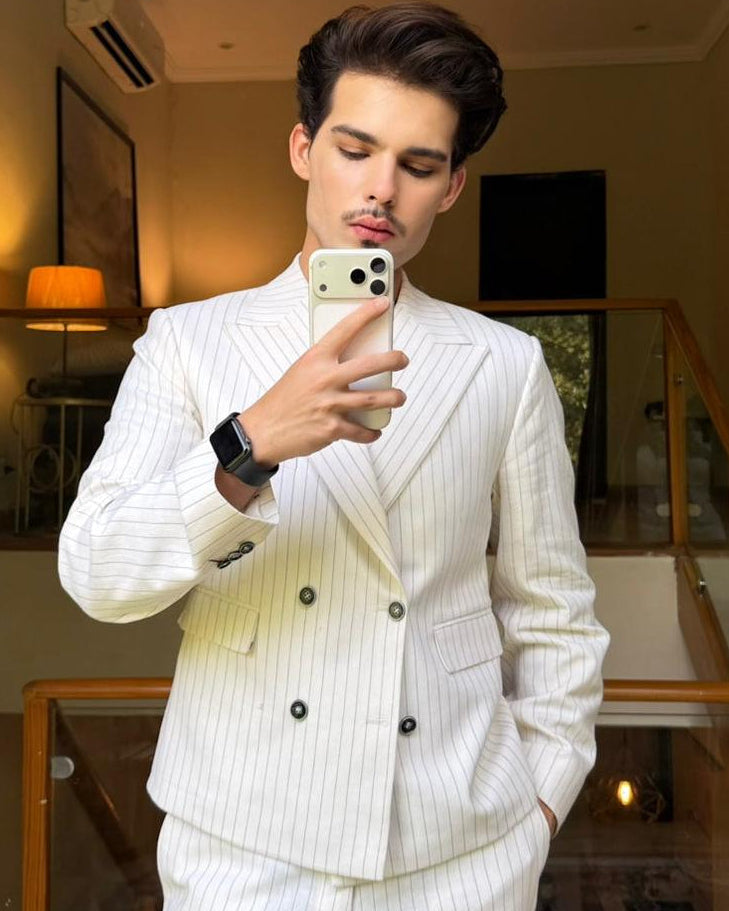 Our client in a white pinstripe suit taking a mirror selfie indoors.