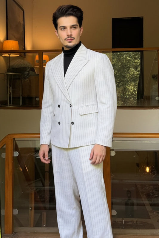 Man taking a mirror selfie wearing a white suit in a room with greenery outside.